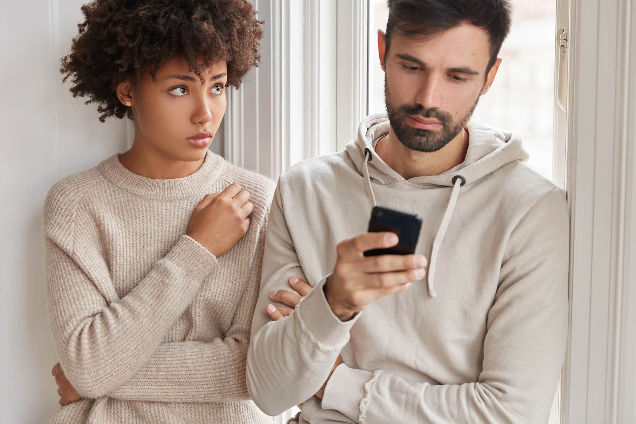 Jealous woman looks at her partner who is ignoring communication, focused into cell phone.