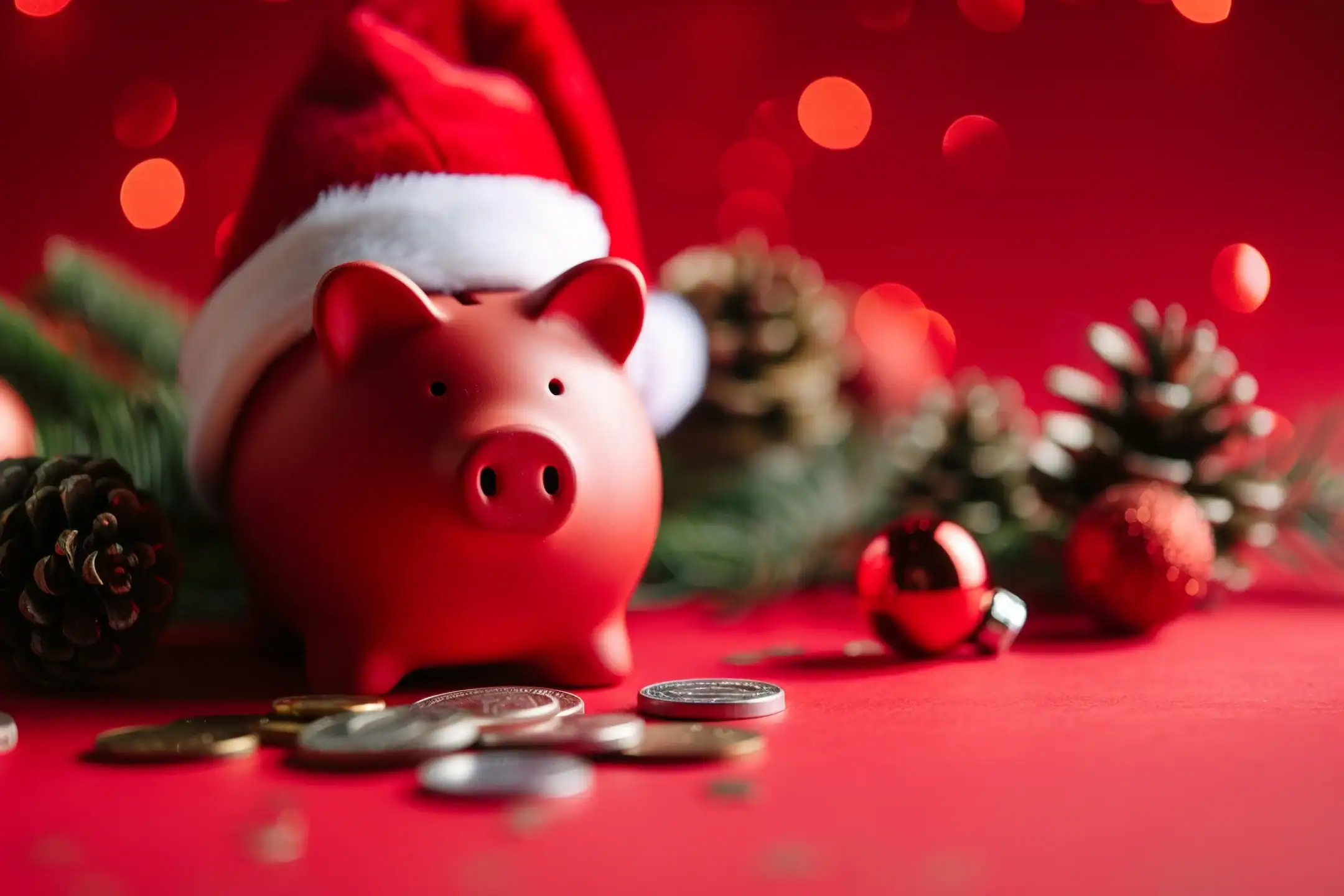 Red piggy bank wearing a Christmas hat and coins in front.